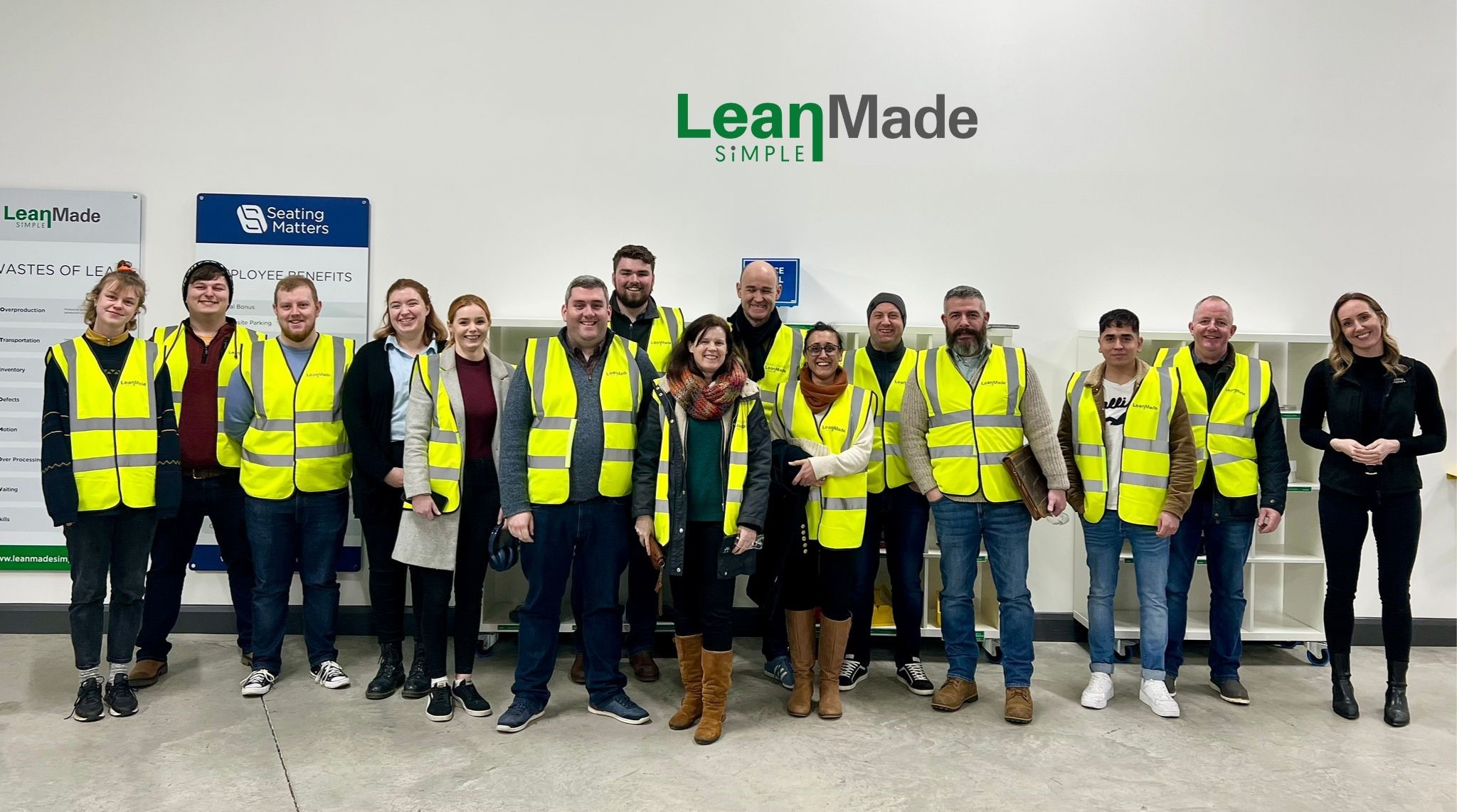 A group of staff and students line up against a white wall that has the words lean made simple on it.